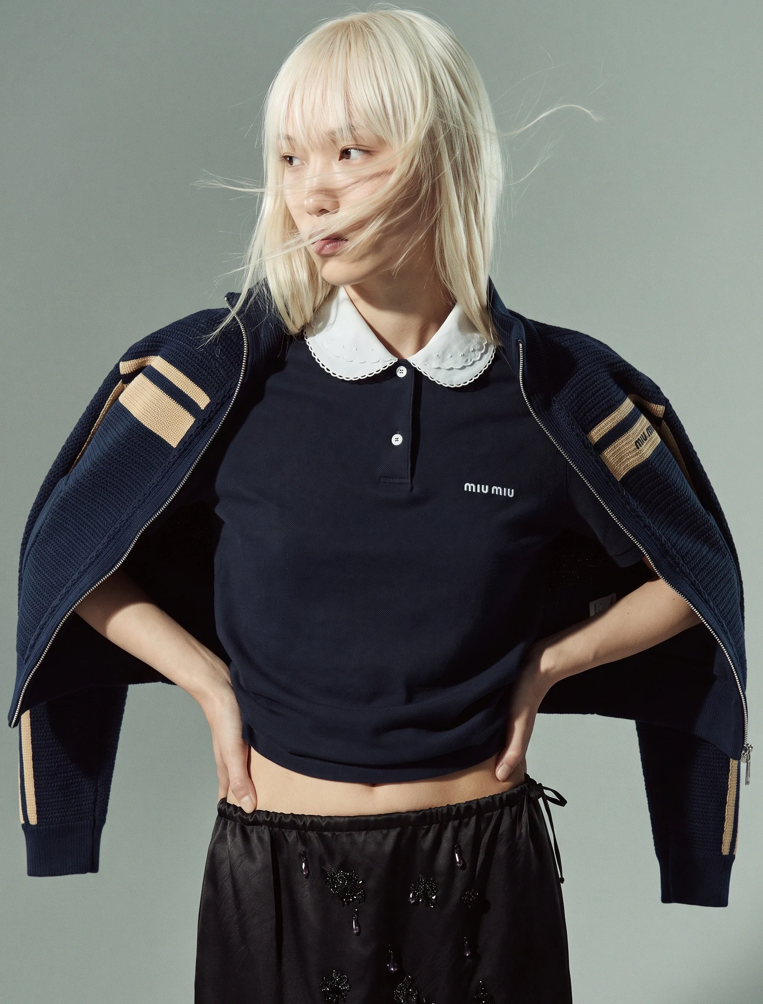 AI-generated on-model image: navy varsity jacket and polo against a sage backdrop