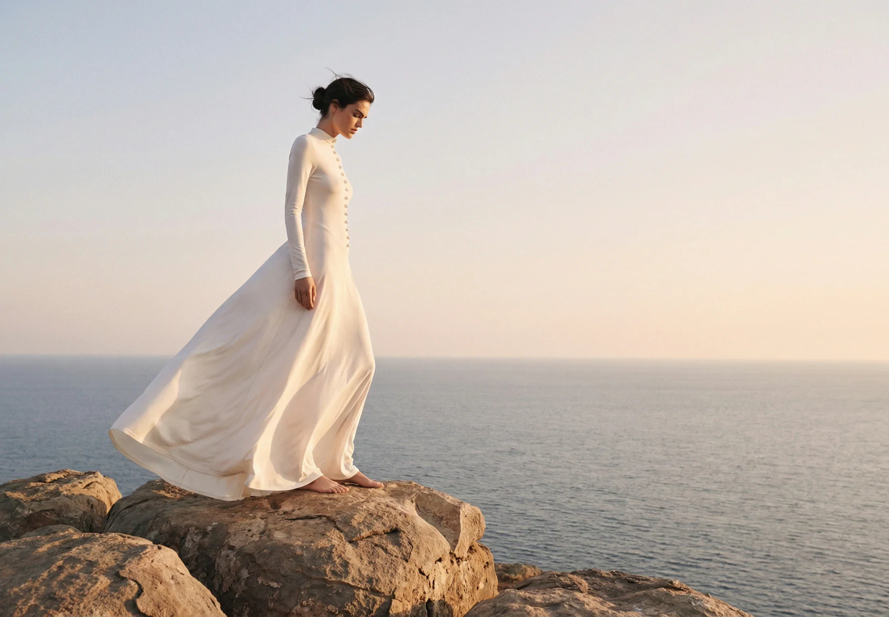 AI-generated on-model image: white dress photographed walking on coastal rocks at dusk, wide frame