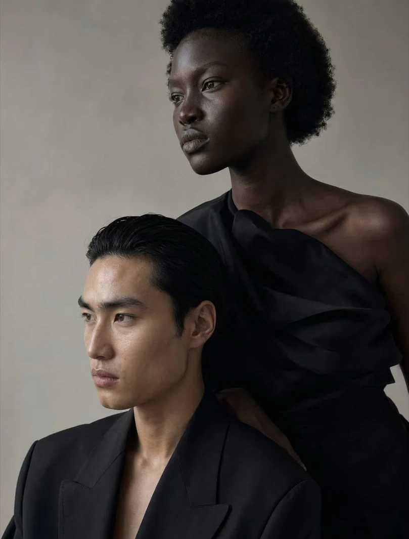AI-generated on-model image: two models in black tailoring, close-up portrait