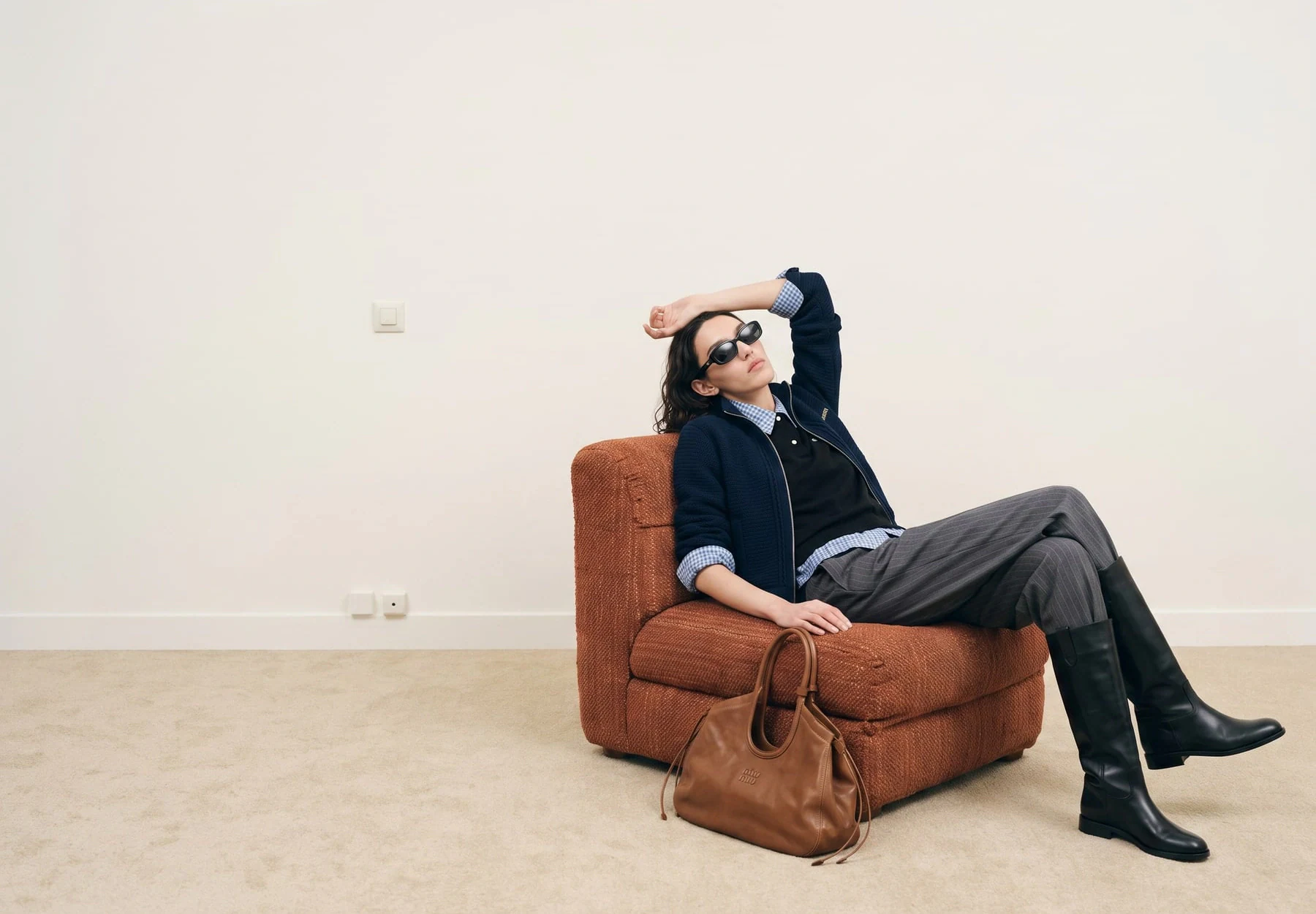 AI-generated on-model image: tailoring photographed seated in an empty interior, wide frame